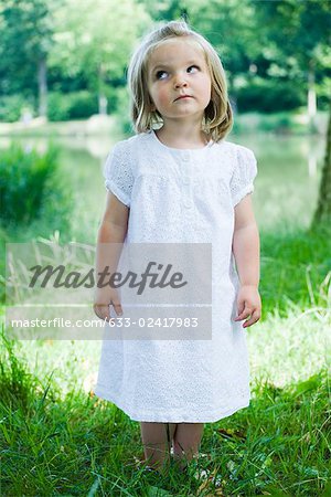 Little girl standing on grass, looking up