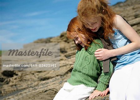 Girl hugging young sister on rocks