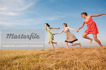 Teenage girls running across a hay field