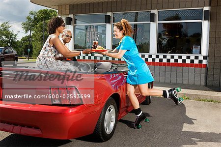 Kellnerin auf Rollerskates servieren Paar im Cabrio im Drive-In Diner