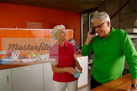 Senior couple in domestic kitchen, man phoning