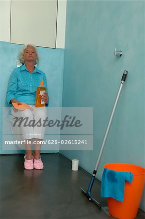 Haute femme à côté de nettoyage des ustensiles assis sur la toilette