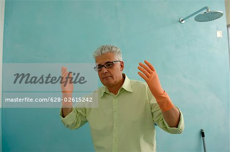 Senior man next to a shower lifting up his hands with rubber gloves on