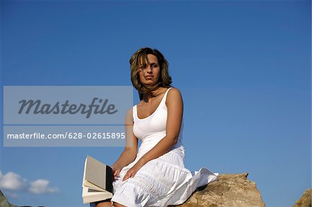 Frau sitzend auf einem Felsen mit einem Buch