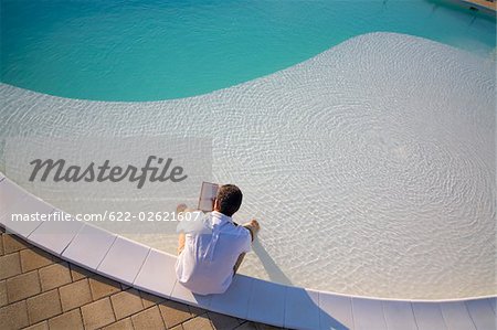 Homme assis au bord de la piscine et en lisant le livre