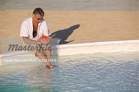 Man sitting at edge of pool and reading book