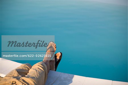 Homme avec flip flops assis au bord de la piscine