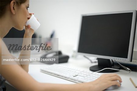 Woman working at desk, drinking from disposable cup