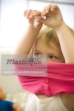 Little girl putting on shirt, arms raised