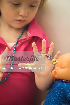 Little girl wearing plastic rings on every finger, looking at hand