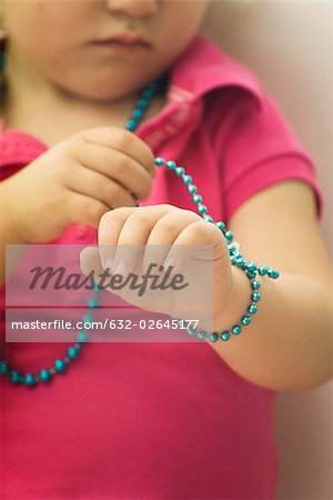Little girl wrapping beaded necklace around wrist, cropped