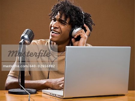 jeune homme dans une chemise marron sur un ordinateur portable avec des écouteurs et un microphone.