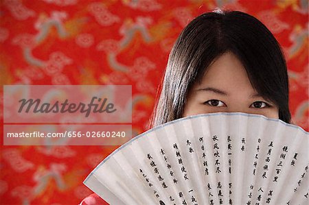 Chinese woman looking over hand-held fan with Chinese characters