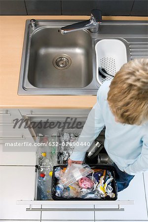 Child placing plastic container in trash can rather than nearby recycling bins