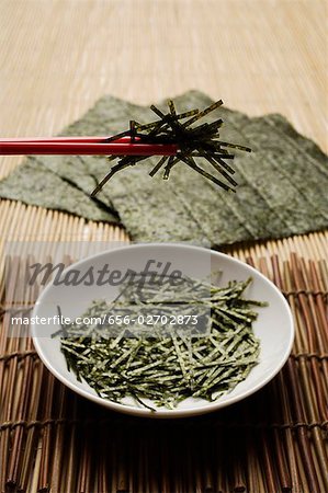 seaweed shreds picked up by red chopstick closeup with seaweed sheets in background