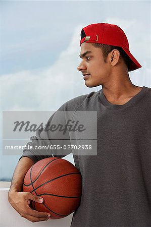 junger Mann mit roter Mütze, hält basketball