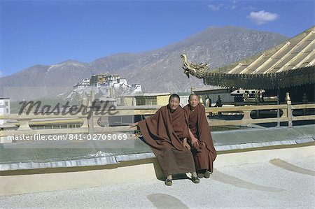 Two Tibetan Buddhist monks at Jokhang temple, with the Potala palace behind, Lhasa, Tibet, China, Asia