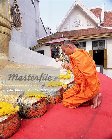 Buddhist monk kneeling and praying at the feet of a standing Buddha, Wat Intharawihan, Bangkok, Thailand, Southeast Asia, Asia
