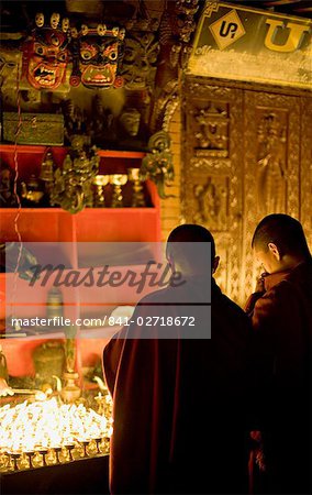 Mönche, die leichte butter Lampen in eine verheißungsvolle Nacht, beobachtet von zwei furchterregende Masken, Boudha Stupa Bodhnath, Kathmandu, Nepal.
