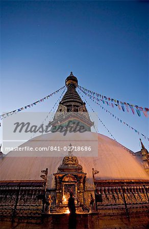 A monk lights butter lamps on gilded shrine at base of stupa at dawn, Swayambhunath (Swayambhu) (Monkey Temple) Buddhist stupa on a hill overlooking Kathmandu, UNESCO World Heritage Site, Nepal, Asia