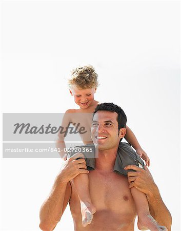 Son (6-8) sitting on father's shoulders on beach