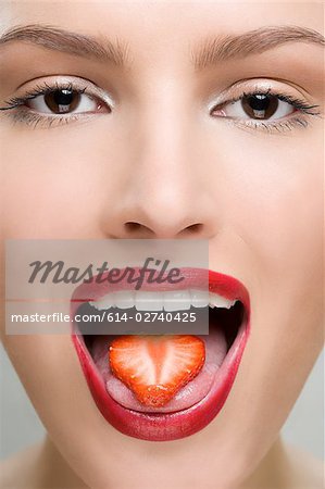 Woman with a slice of strawberry on her tongue