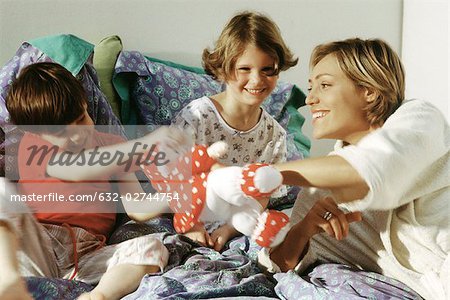 Famille jouant avec animal en peluche dans son lit, souriante