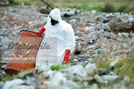 Personne en tenue de protection transportant des barils de déchets dangereux