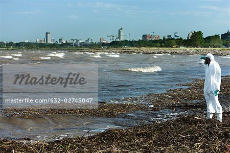 Person in protective suit standing on polluted shore, city in background