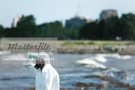 Person in protective suit looking at polluted water, side view