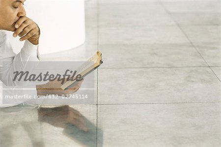 Senior man lying on tiled floor reading book