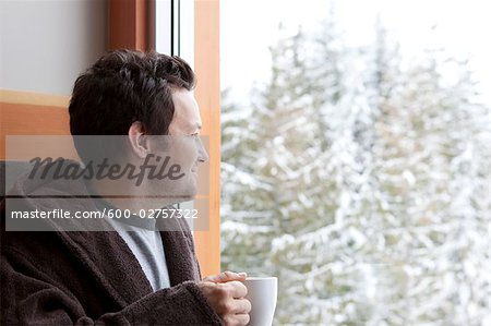 Man in Bathrobe Holding a Cup of Coffee and Gazing Out the Window