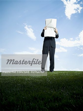 Businessman standing on the grass and reading a newspaper