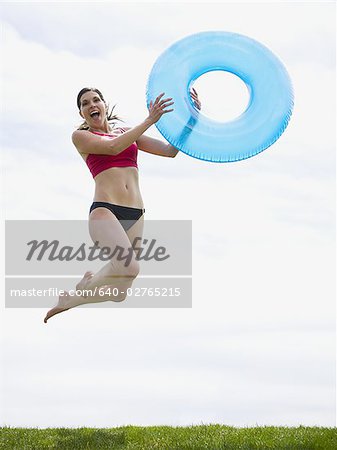 Woman in bikini jumping and smiling with swimming ring