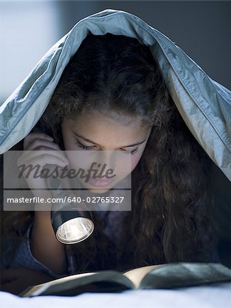 Fille pose dans son lit sous couverture avec lecture de lampe de poche