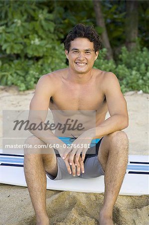 Portrait d'un jeune homme assis sur une planche de surf et souriant