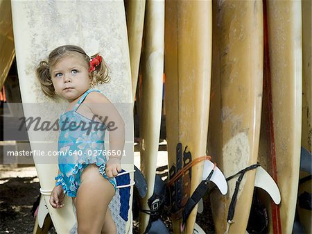 Portrait of a baby girl leaning against a surfboard