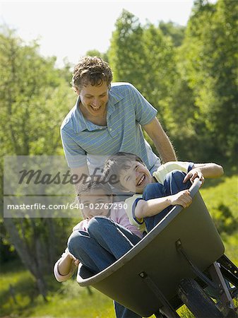 man pushing his son and daughter in a wheelbarrow