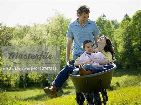 man pushing his daughter and his wife in a wheelbarrow