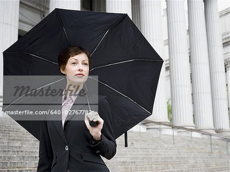 Portrait of a female lawyer standing on the steps of a courthouse and holding an umbrella