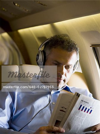 Un homme d'affaires, écouter de la musique sur le casque et en lisant un magazine dans un avion