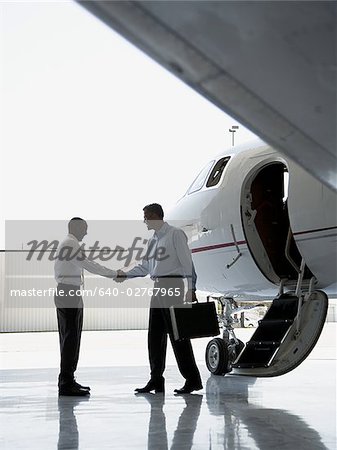 Voir le profil:: deux hommes d'affaires, serrant la main près d'un avion