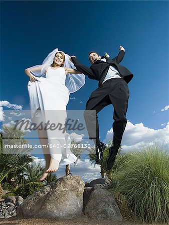 Low angle view of a newlywed couple holding hands and jumping