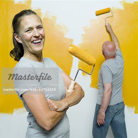 Portrait d'une femme senior tenant un rouleau de peinture avec un homme senior en peignant un mur