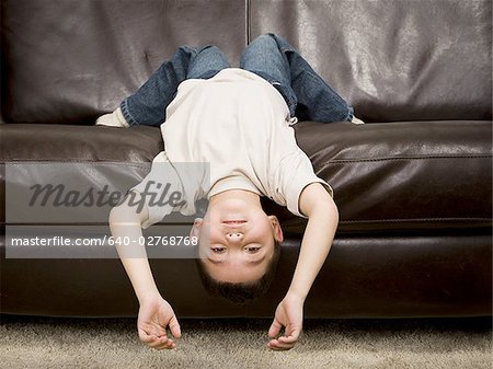 Jeune garçon couché à l'envers sur un sofa en cuir