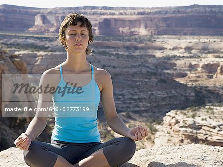 Woman sitting cross legged on rock outdoors doing yoga