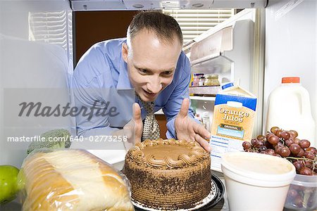 Homme au réfrigérateur tremper le doigt dans le gâteau au chocolat