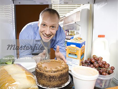 Mann im Kühlschrank Eintauchen der Finger in Schokoladenkuchen