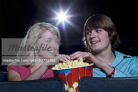 Garçon et fille de toucher les mains dans le pop corn au cinéma
