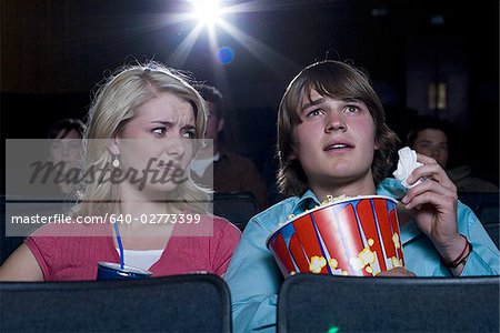 Boy with tissues crying at movie theater with girl watching